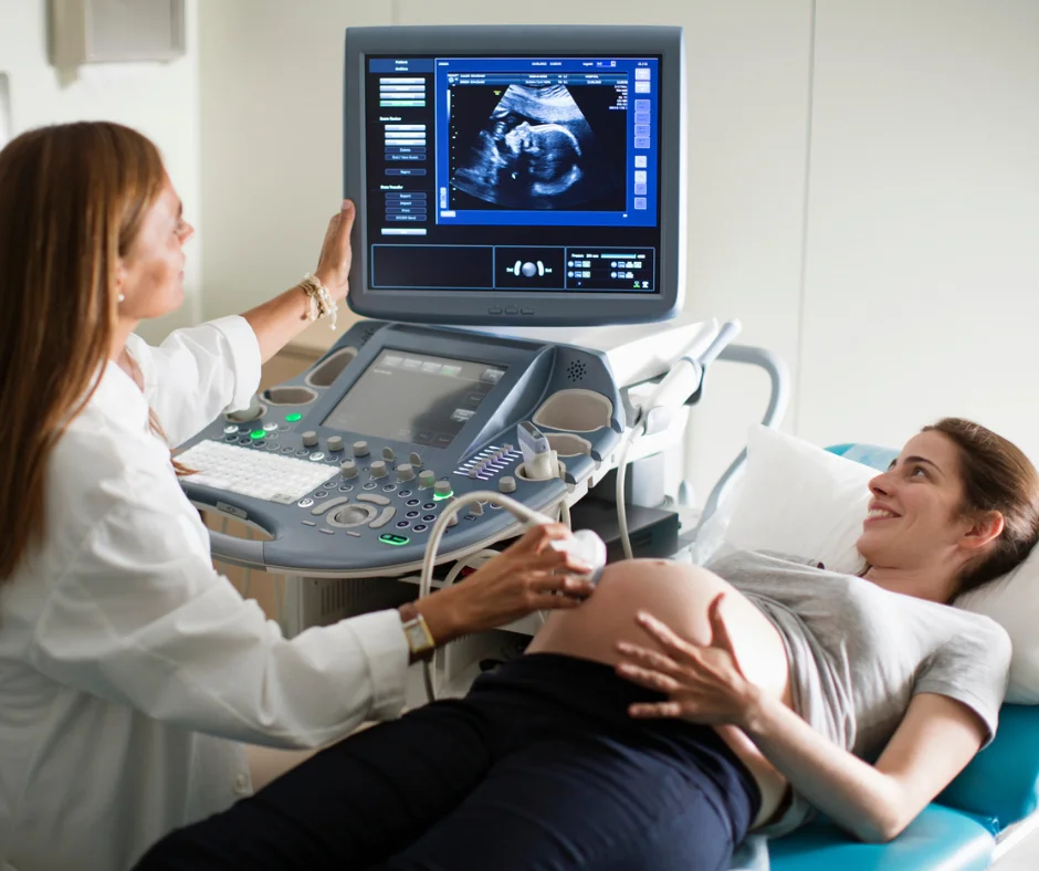 Gestante sorrindo durante exame de ultrassom, com o médico mostrando as imagens no monitor