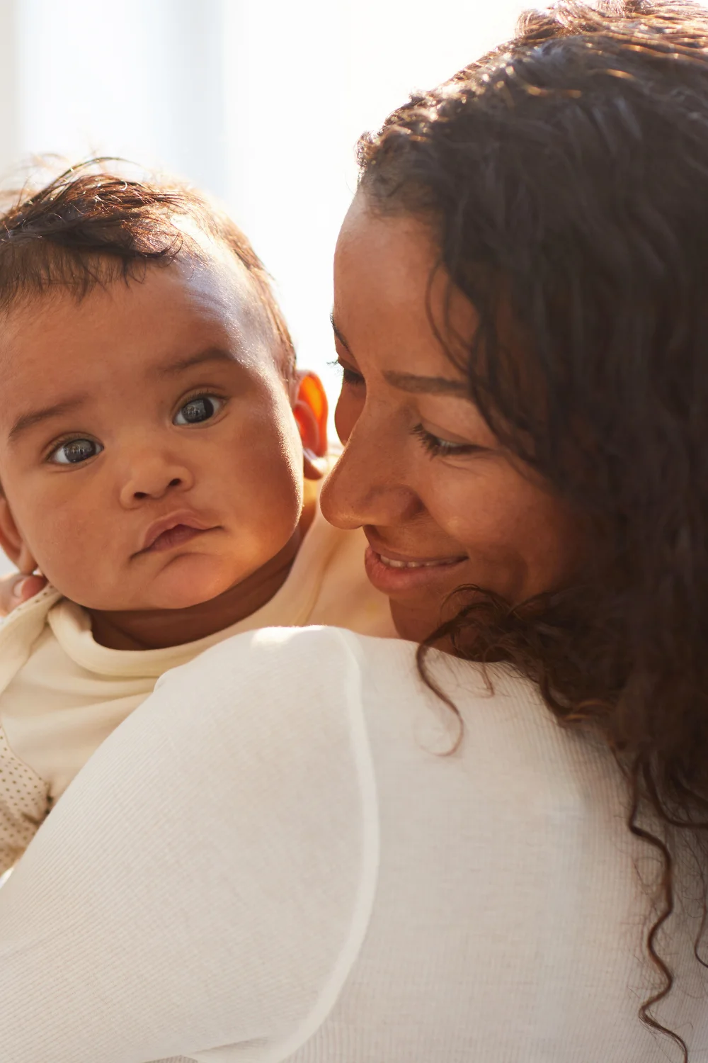 Mulher brasileira sorrindo enquanto olha para seu bebê de 1 ano