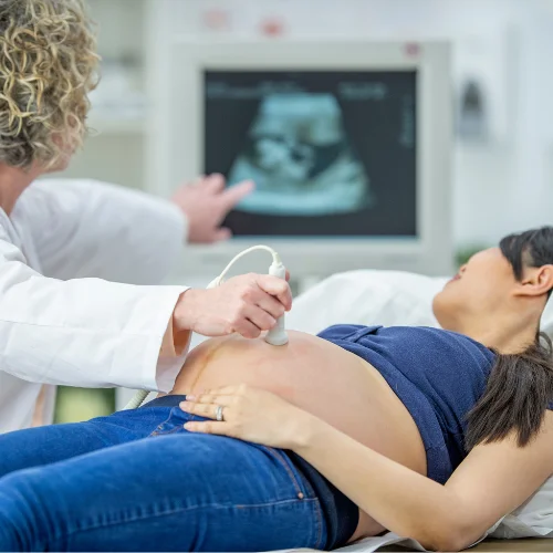 Médico realizando ultrassom em gestante deitada, observando o monitor com atenção